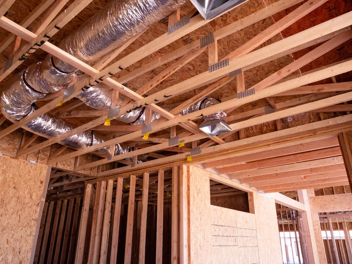 Insulated flexible ducts running between the roof trusses of a timber-framed house under construction