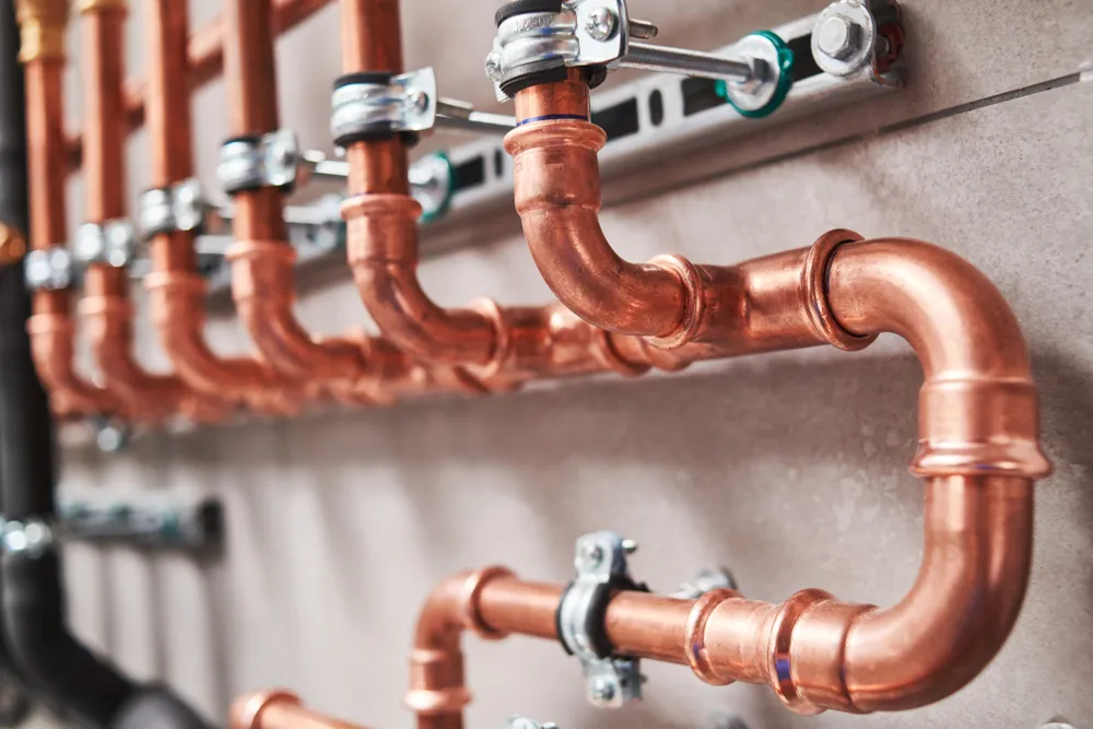 Copper piping held by pipe clamps along a wall