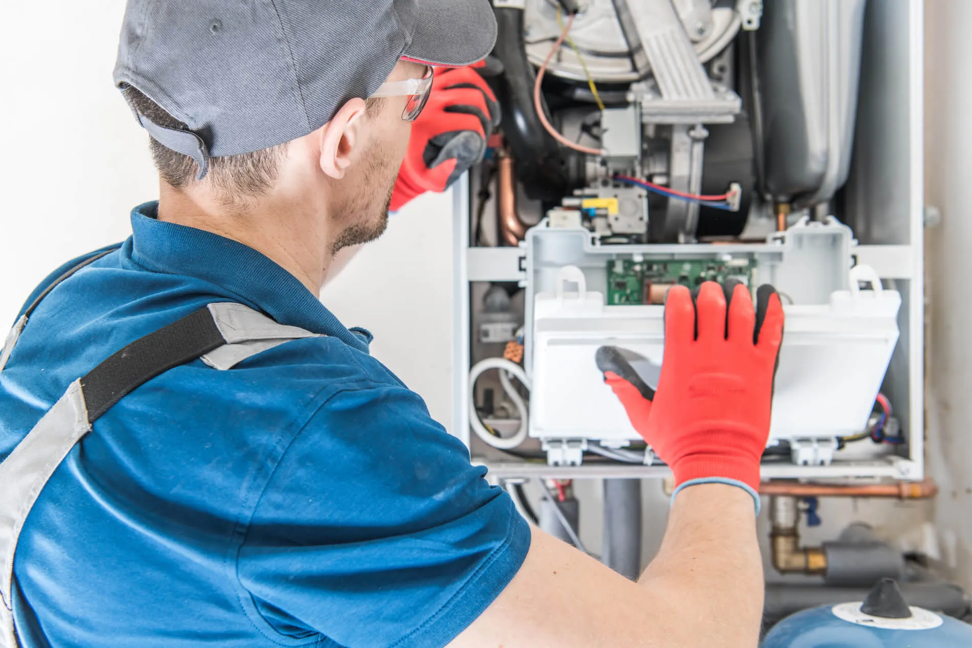 Technician in red work gloves working on the control board of an open gas heating unit